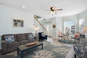 A living room with a sofa, coffee table, and chairs, a staircase, and a view through the windows. - 5 Buoys: Ocean View House Near Ocean Crest Pier (Oak Island)
