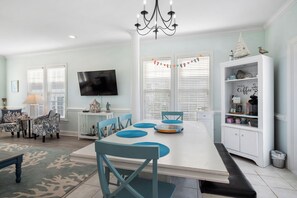 A dining area with a white table, blue chairs, a chandelier, and a television on the wall.