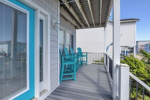A covered outdoor deck with a railing, a set of chairs, and a view of a residential building in the background.