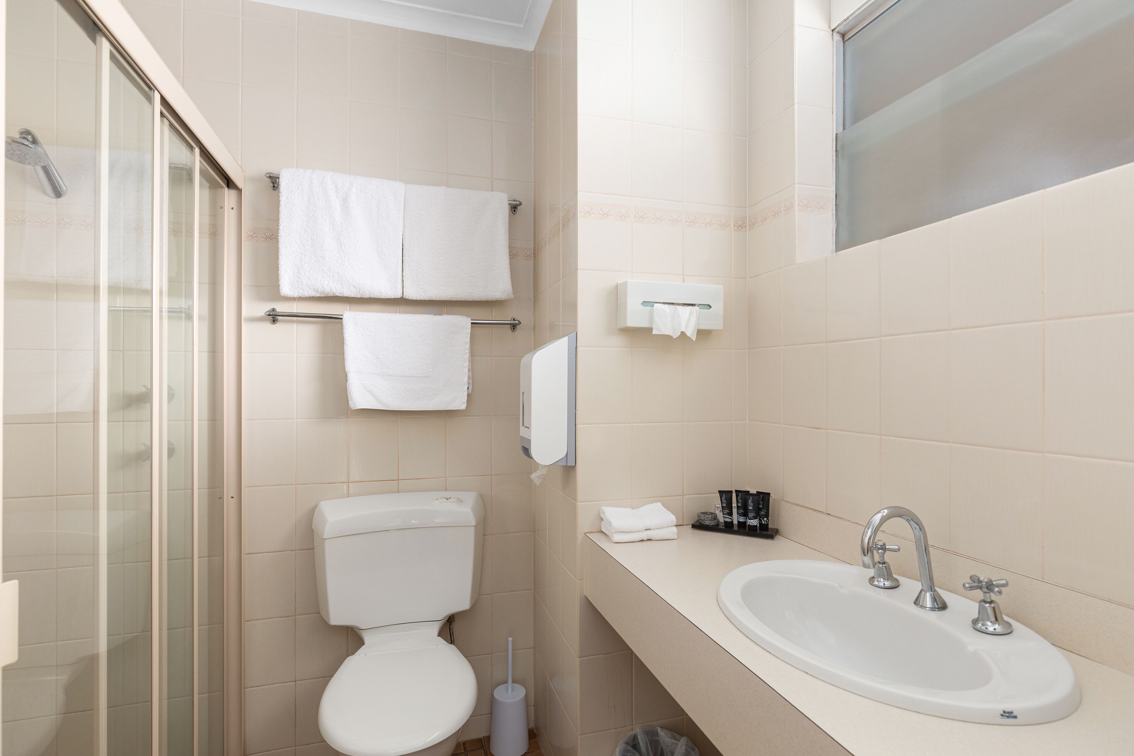A bathroom with a toilet, sink, and glass shower enclosure.