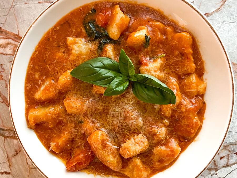 A bowl of pasta with a tomato-based sauce, garnished with basil and grated cheese.