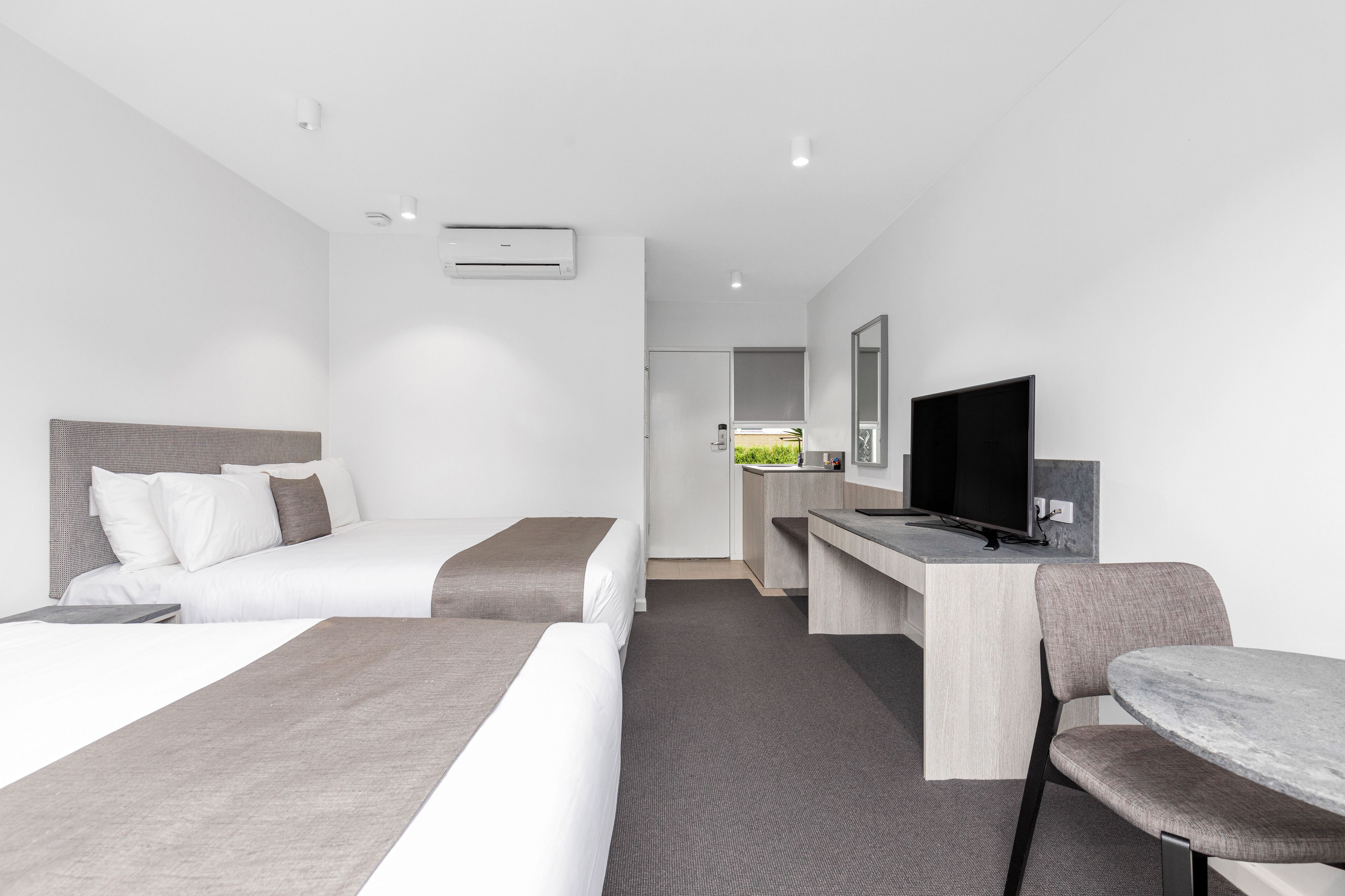 A hotel room with two beds, a desk with a TV, and a bathroom visible in the background.