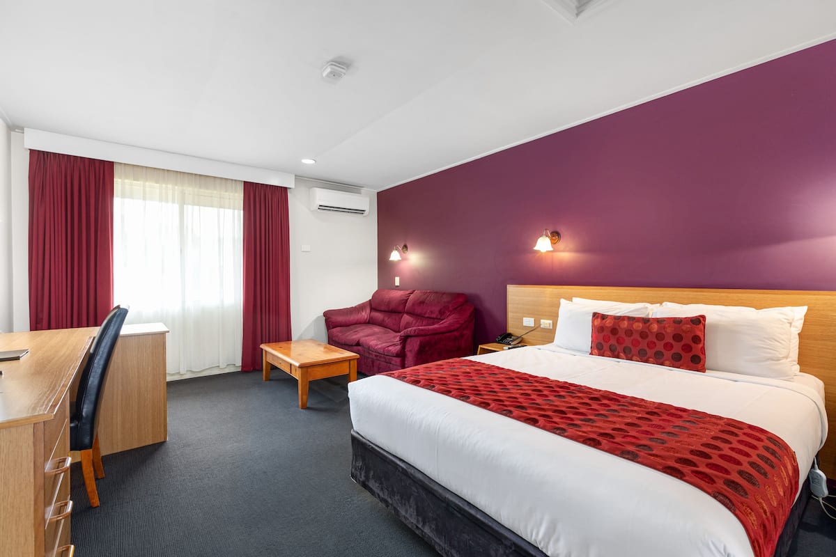 A hotel room with a bed, a desk, a chair, a small table, and a couch.