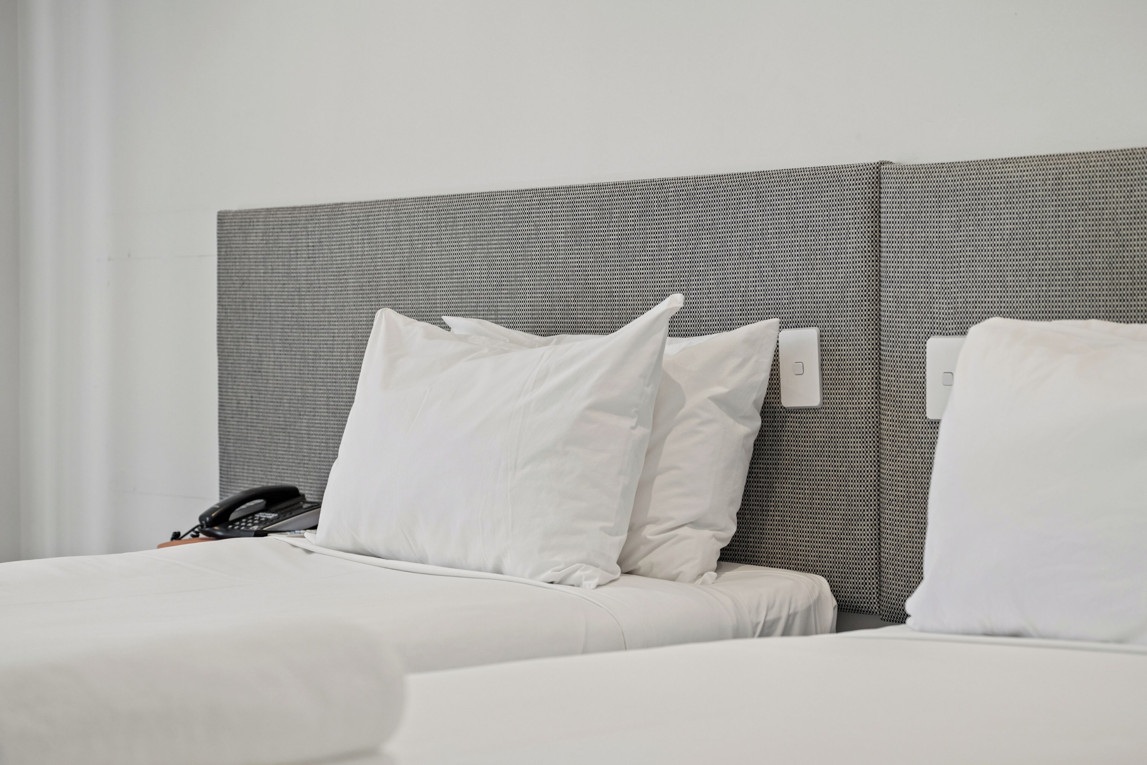 Habitación de hotel con cama, almohadas, teléfono y un interruptor de luz en la pared.