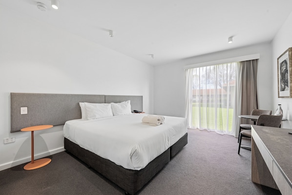 Una habitación de hotel con una cama grande, un escritorio, una silla y un ventanal con cortinas.