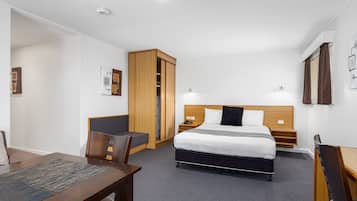 Une chambre d’hôtel comprenant un lit, un bureau, une chaise, une armoire et une petite table.