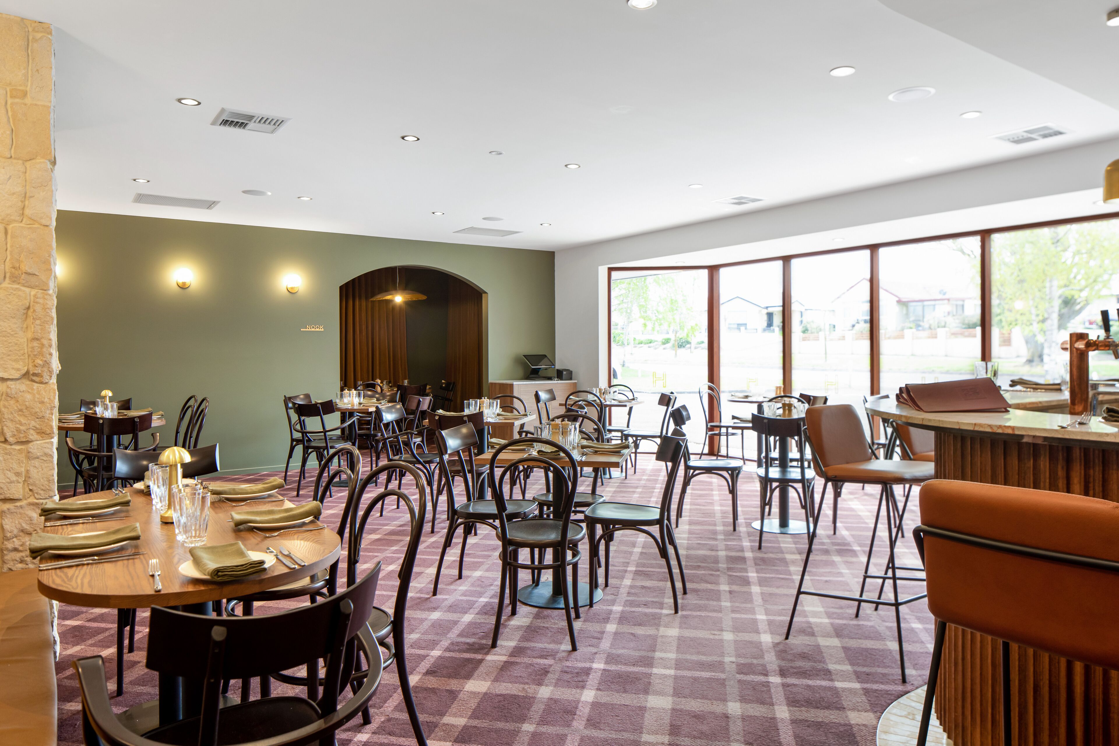 A restaurant with multiple dining tables and chairs, a checkered floor, and large windows allowing natural light.