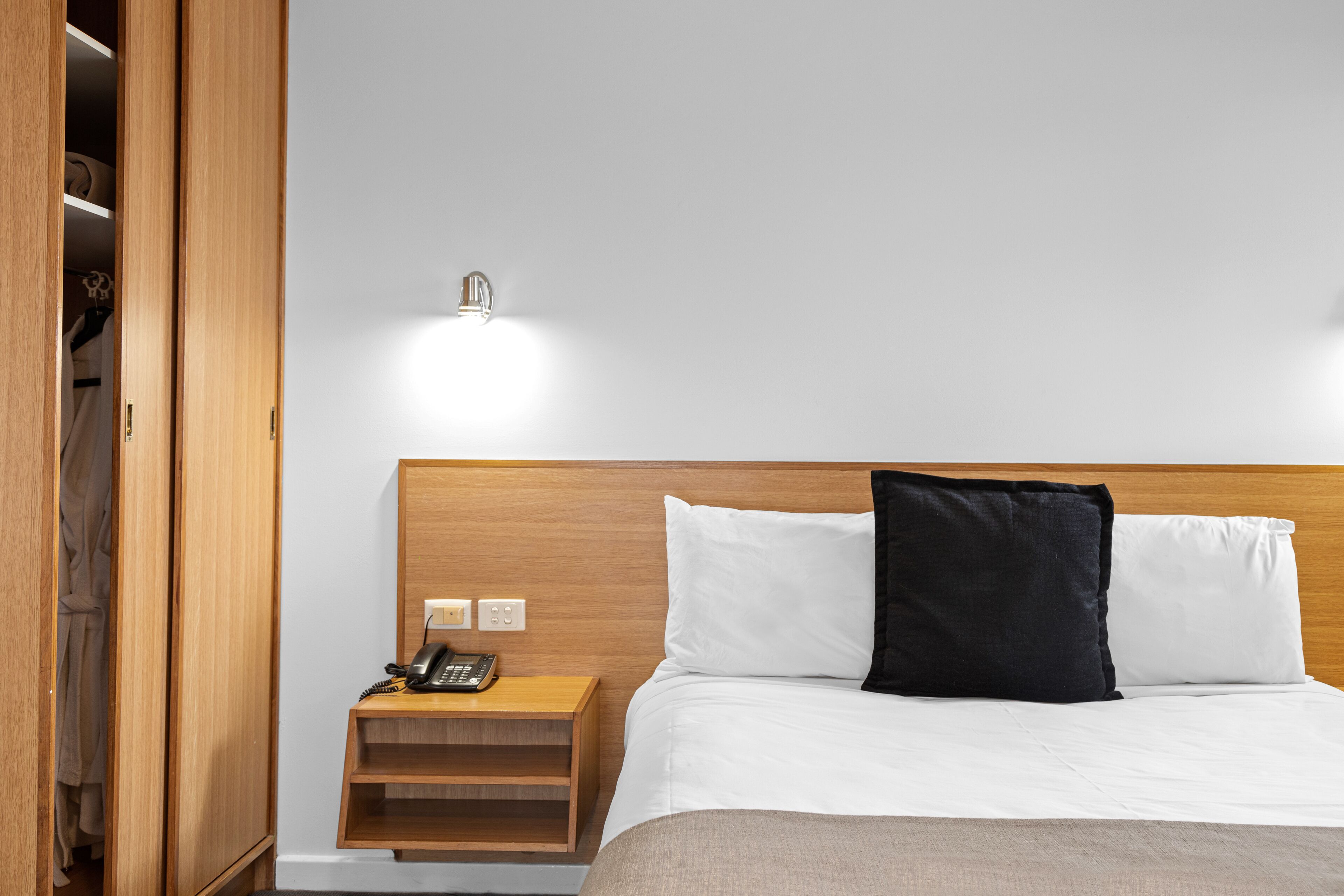 A hotel room with a wooden headboard, a bedside table with a phone, and a nightstand.