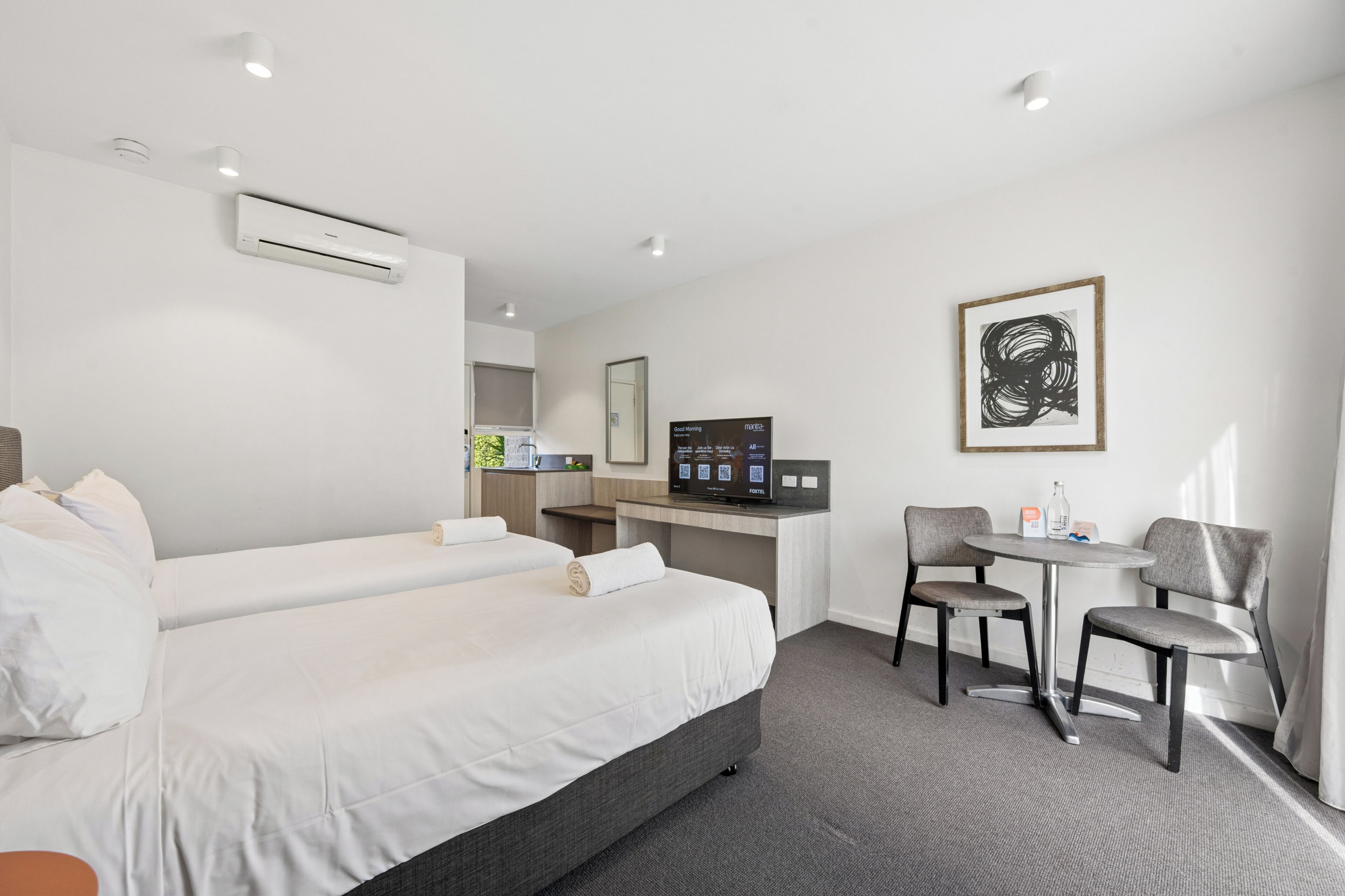 A hotel room with a bed, a desk, a chair, and a small table.
