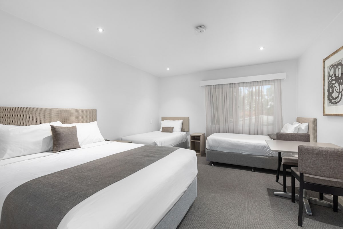 A hotel room with two single beds, a desk, and a chair.