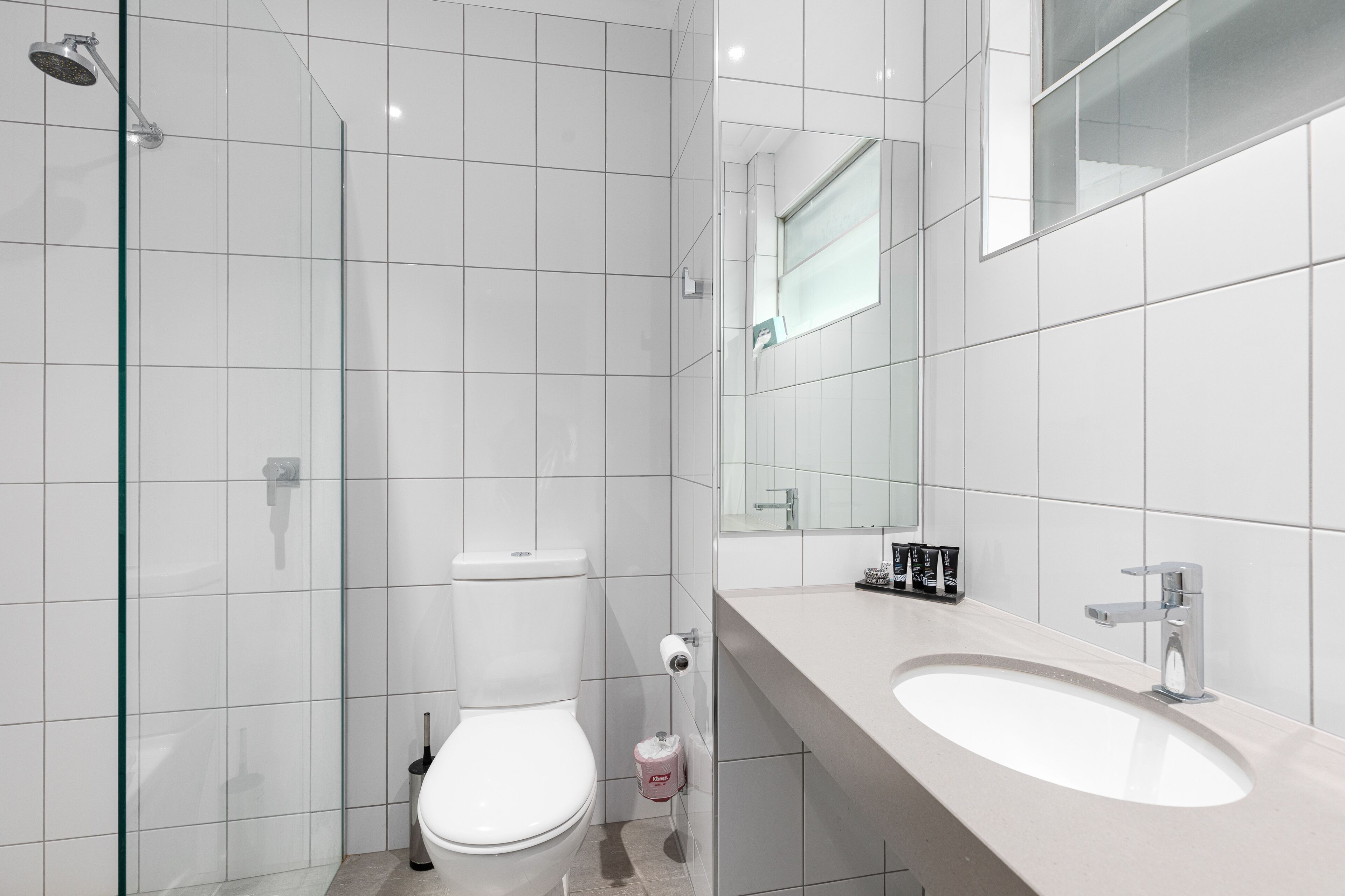Ein modernes Badezimmer mit einer Duschkabine aus Glas, einer weißen Toilette und einem großen Waschbecken mit Spiegel darüber.