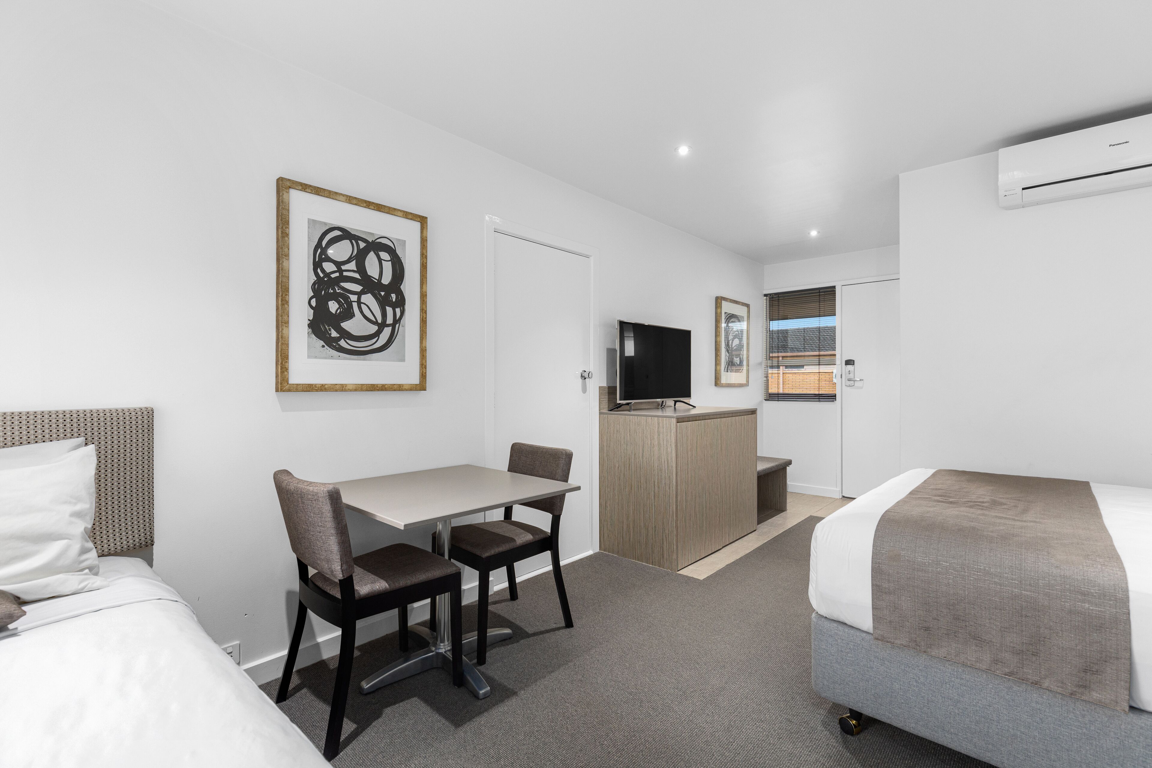 Een hotelkamer met een bed, een bureau met twee stoelen, een televisie en een lijst met abstracte kunst aan de muur.