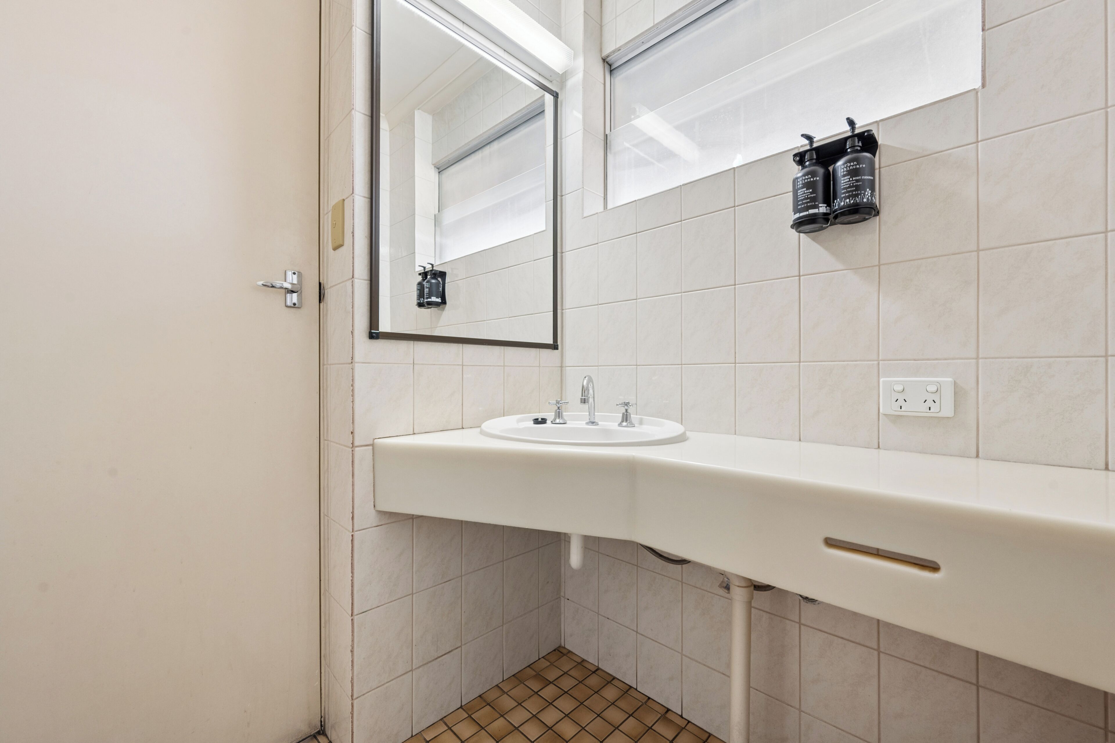 A bathroom with a white sink, a mirror, and two black toiletry bottles on the wall.