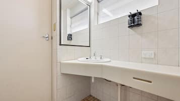 A bathroom with a white sink, a mirror, and two black toiletry bottles on the wall.