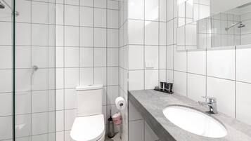 A modern bathroom with white tiles, a glass shower enclosure, a toilet, and a granite countertop with a sink and mirror.