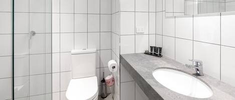 A modern bathroom with white tiles, a glass shower enclosure, a toilet, and a granite countertop with a sink and mirror.