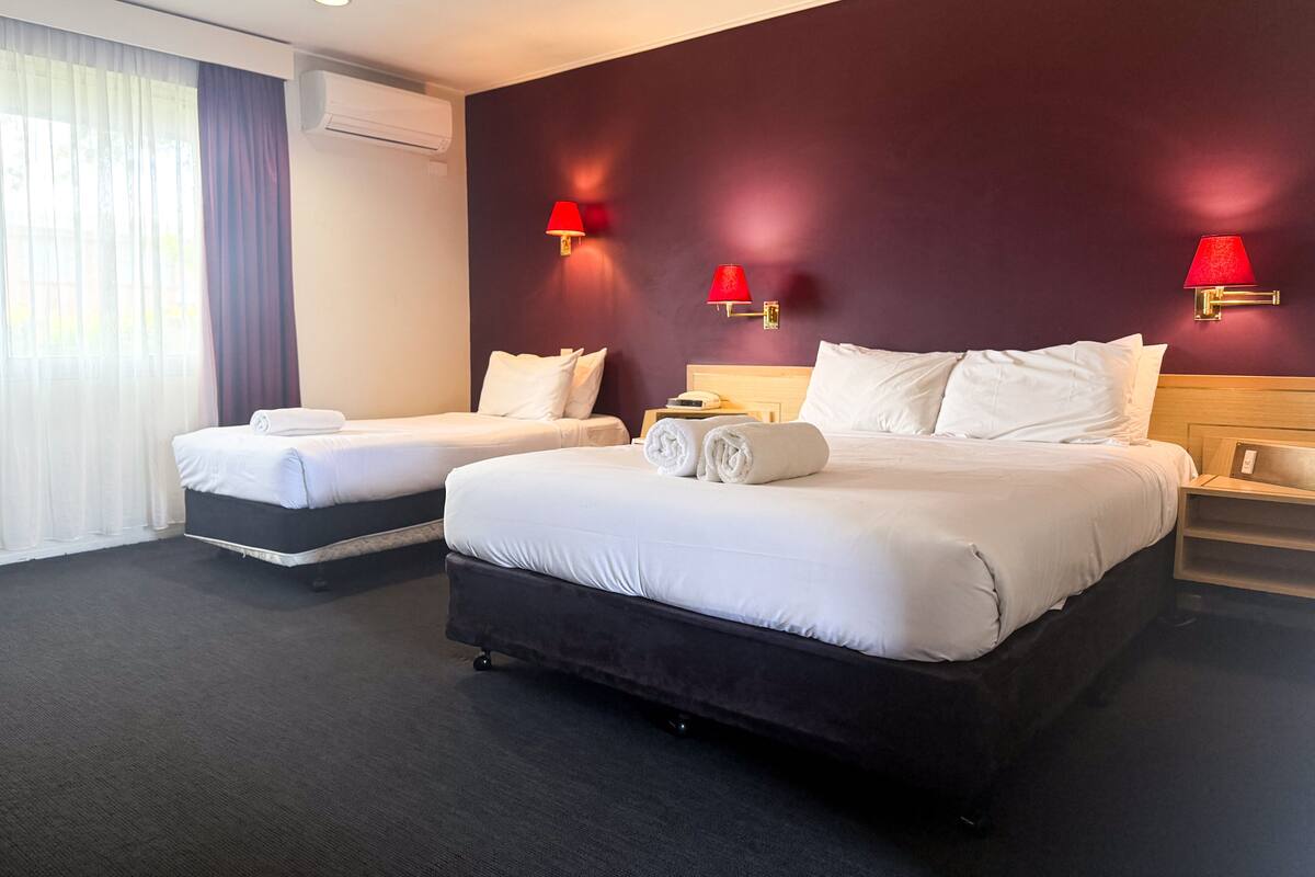 A hotel room with two beds, a dark carpet, and red wall sconces.