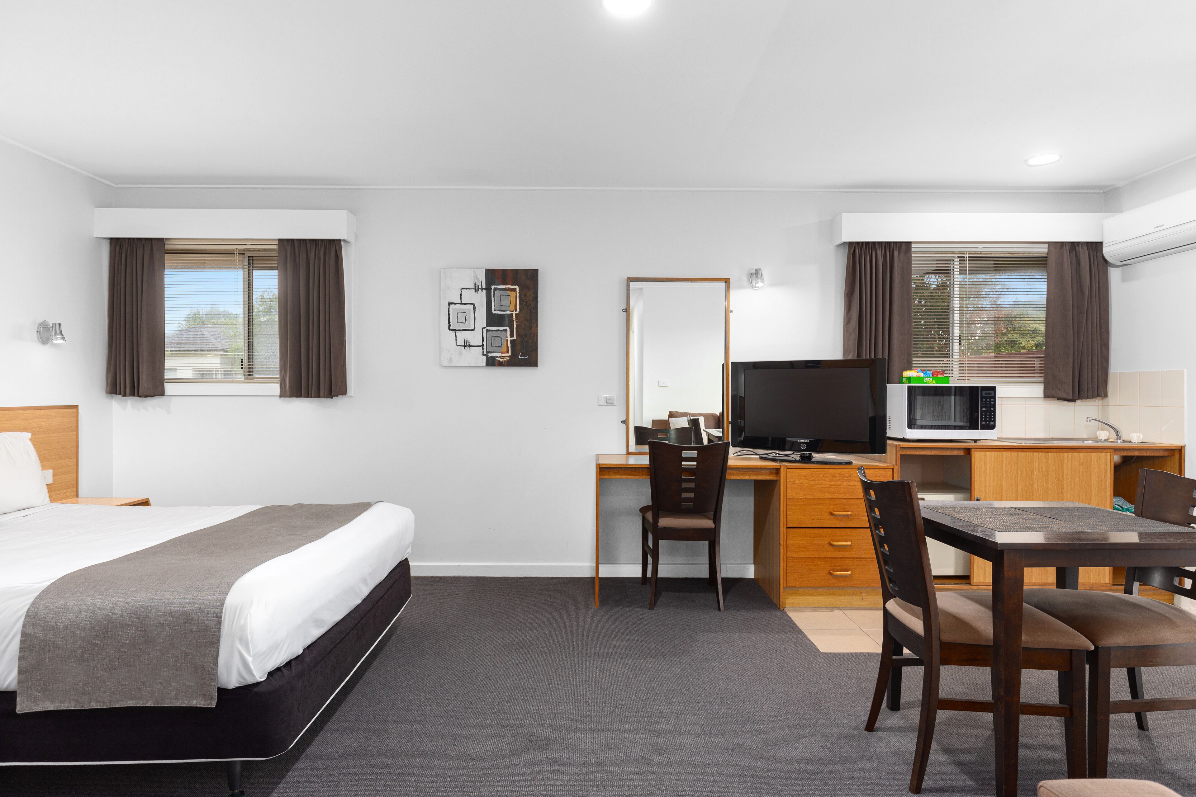 A hotel room with a bed, desk, chair, and kitchenette.