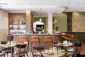 Un restaurante con una zona de bar, varias mesas con sillas y una pared de piedra.