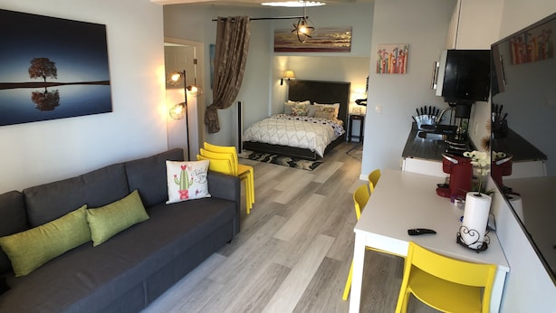 A modern, compact living space with a bed, a sofa, a dining area, and a kitchenette.