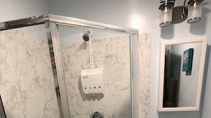 A bathroom with a glass-enclosed shower, a sink with a black faucet, and a marble-patterned wall.