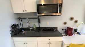 A compact kitchen with white cabinets, a black countertop, a stainless steel microwave, and a coffee maker.