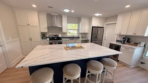 Een moderne keuken met witte kastjes, een groot marmeren eiland met barstoelen en geïntegreerde apparatuur.