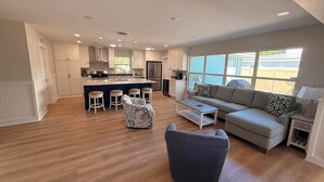 Een moderne keuken met witte kasten, een centraal eiland met krukken, een grijze bank en een gestreept fauteuil.