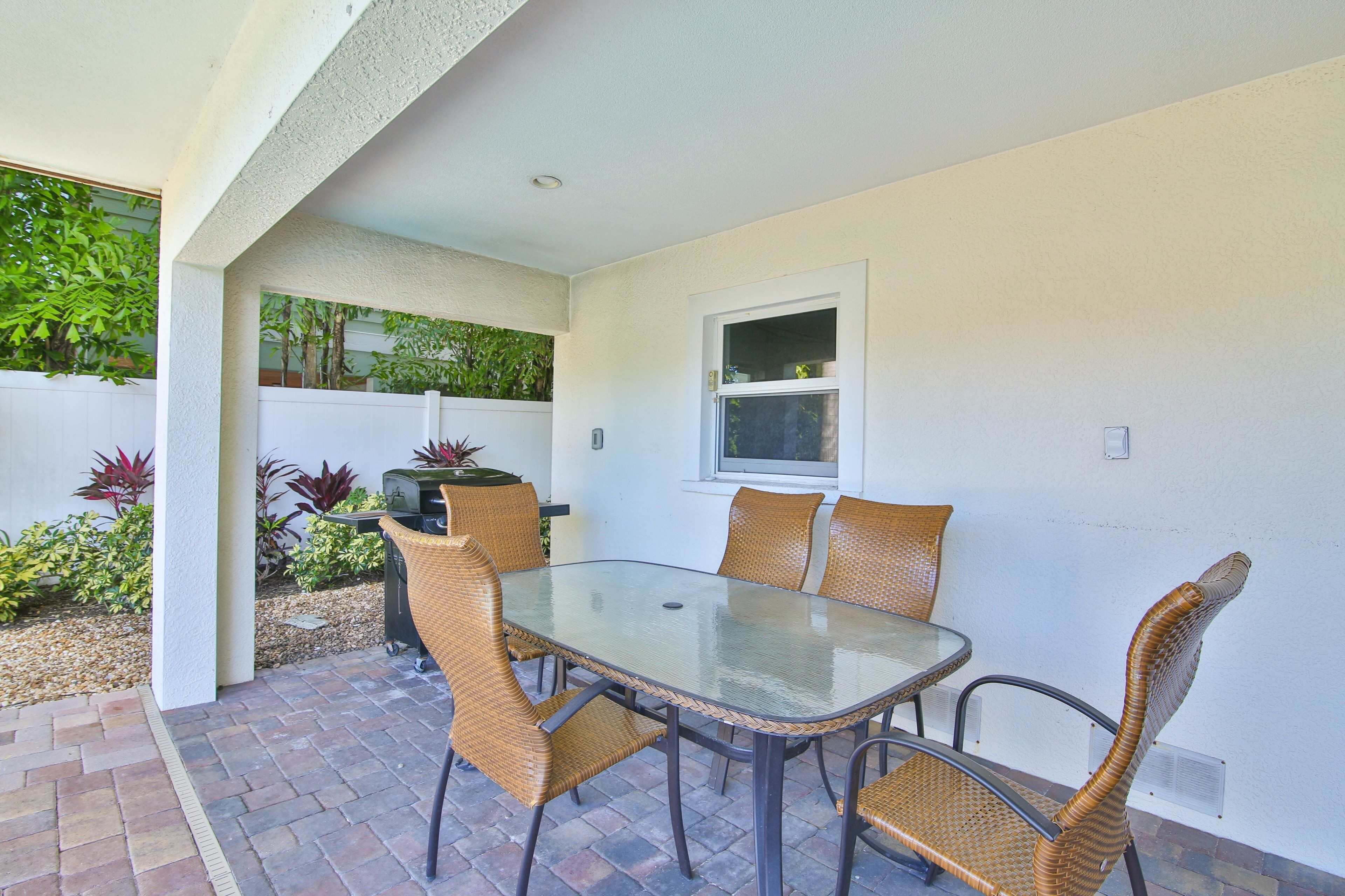 A patio with a glass table and wicker chairs, surrounded by a white wall and a small window.
