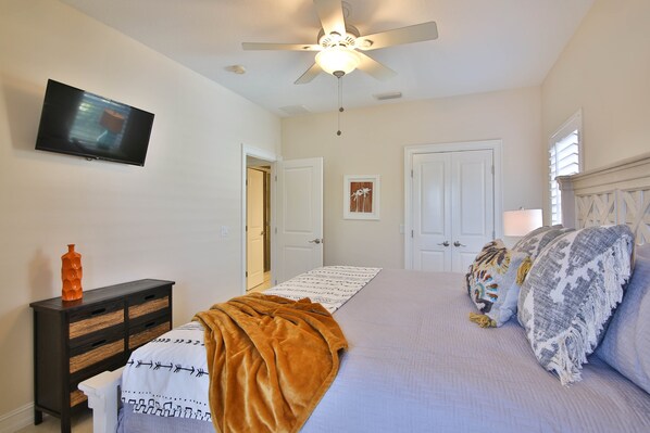 A bedroom with a bed, a television, a ceiling fan, and a door.