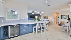 A modern kitchen with a central island, built-in appliances, and a dining area with white chairs. - Luxury waterfront home with a heated pool and spa! (Anna Maria)
