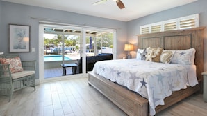 A bedroom with a large bed, a ceiling fan, a view of a pool, and a chair. - 3 bedroom 2 bathroom canal front home with a heated pool located in Anna Maria (Anna Maria Island)
