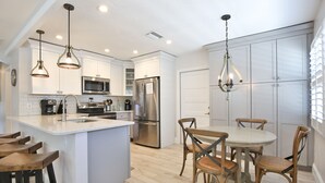 A modern kitchen with white cabinetry, stainless steel appliances, and wooden bar stools. - 3 bedroom 2 bathroom canal front home with a heated pool located in Anna Maria (Anna Maria Island)