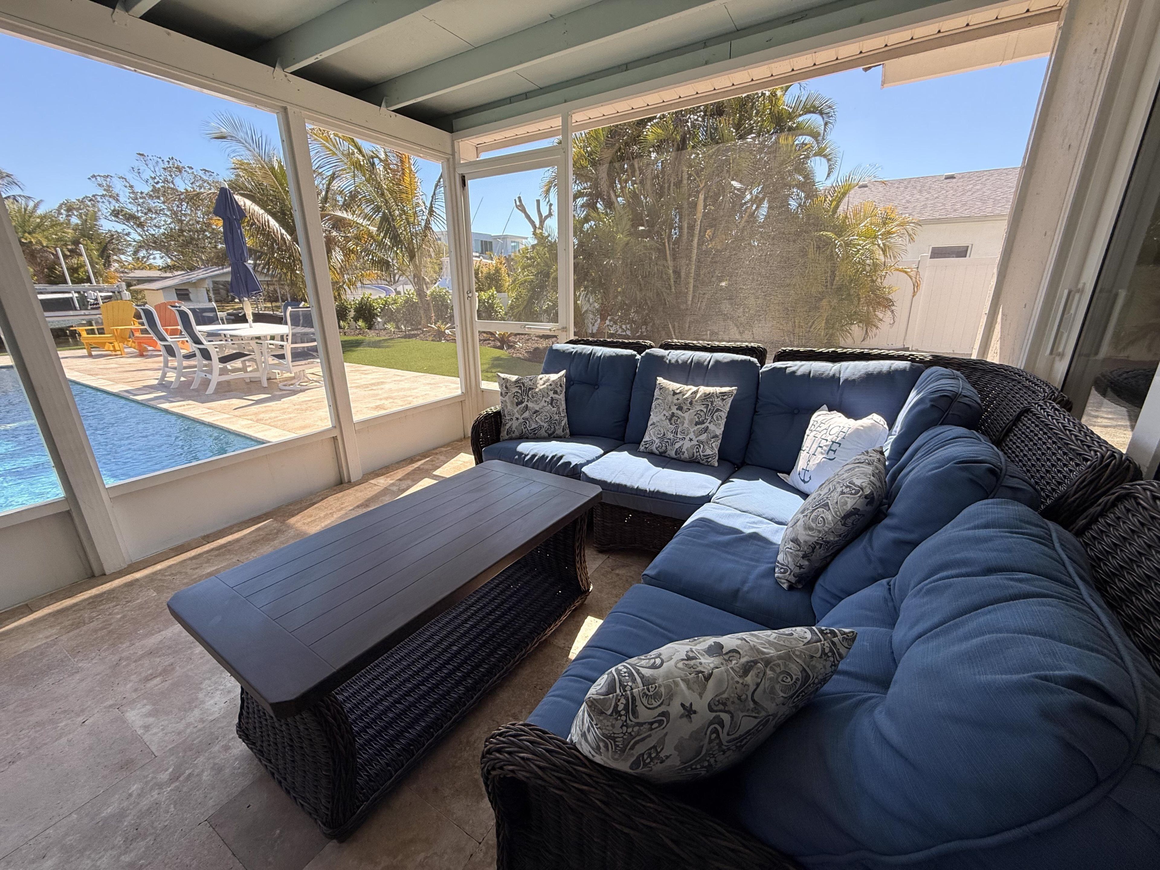 A covered outdoor seating area with a pool, wicker furniture, and a view of the backyard.