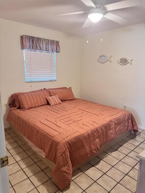 A bedroom with a bed, a ceiling fan, a window with blinds, and two wall decorations. - Delightful, comfortable villa just steps from the beach! (Holmes Beach)