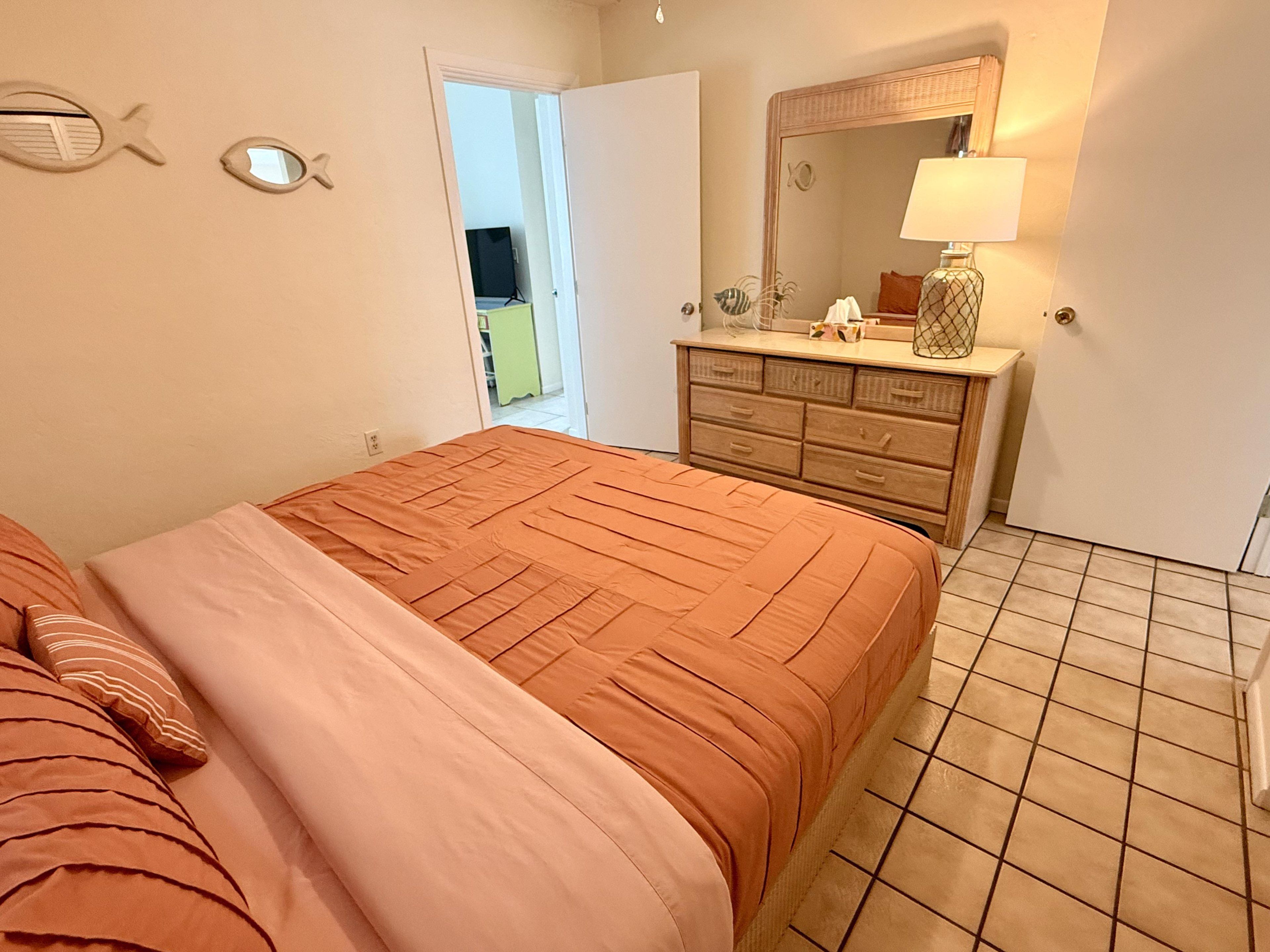 Une chambre à coucher comprenant un lit, une commode, un miroir et une porte donnant sur une autre pièce.