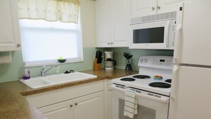 A kitchen with white cabinets, a sink, a stove, a microwave, and a refrigerator. - Delightful, comfortable villa just steps from the beach! (Holmes Beach)