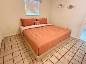 A bedroom with a bed, a window with blinds, and a tiled floor.