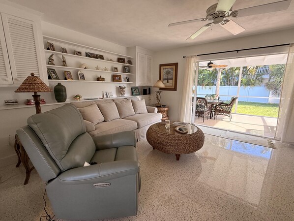 Una sala de estar con sofá, sillón, mesa de centro y objetos decorativos en estanterías.
