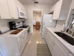 A kitchen with white cabinets, a microwave, a coffee maker, and a refrigerator.