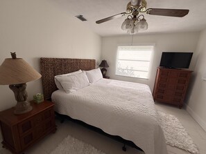 Un dormitorio con cama, ventilador de techo, televisor, mesita de noche y cómoda.