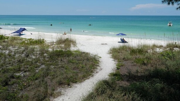 A beach path leading to the sea with umbrellas and a boat in the distance.