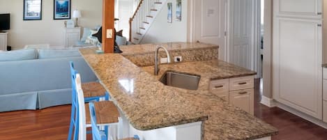 A kitchen with granite countertops, a stainless steel sink, and a bar area with stools.