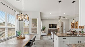 A modern kitchen with a large island, white cabinetry, and pendant lighting. - Stay at Steph’s Farmhouse! Right next to Kalahari Resorts and Dell Diamond! (Round Rock)