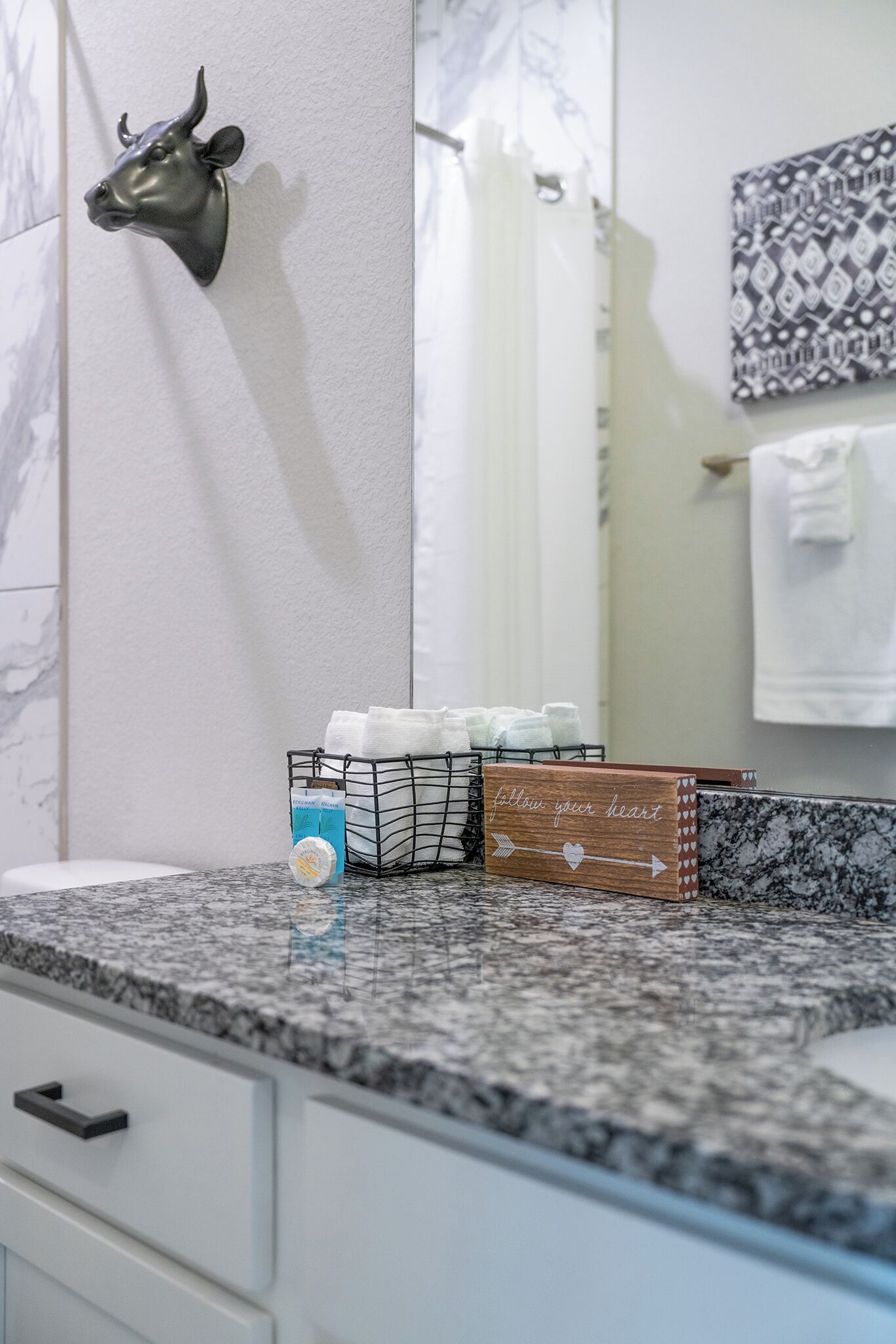 A bathroom with a marble countertop, a bull head decoration, a towel rack, and a mirror.