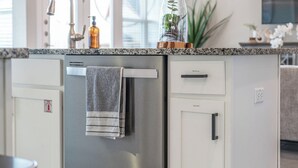 A modern kitchen with a stainless steel refrigerator, a granite countertop, and pendant lighting. - Stay at Steph’s Farmhouse! Right next to Kalahari Resorts and Dell Diamond! (Round Rock)
