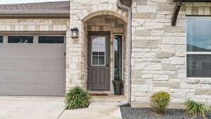 A modern house with a stone facade, a garage, and a well-maintained lawn. - Stay at Steph’s Farmhouse! Right next to Kalahari Resorts and Dell Diamond! (Round Rock)
