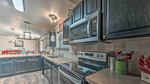 A modern kitchen with dark cabinetry, stainless steel appliances, and a wooden floor. - Wooded Ruidoso Hideaway w/ Deck: Ski, Hike & Golf! (Ruidoso)