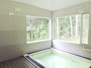 A bathroom with white tiled walls, a bathtub, and large windows offering a view of a forest. - pension AKA-TOMBO (Shinshiro)