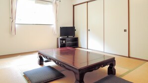 A traditional Japanese room with tatami flooring, a low wooden table, a television, and sliding shoji doors.